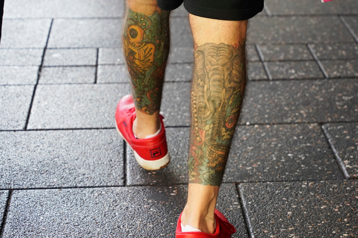 a man with tattoos and red shoes walking down a sidewalk