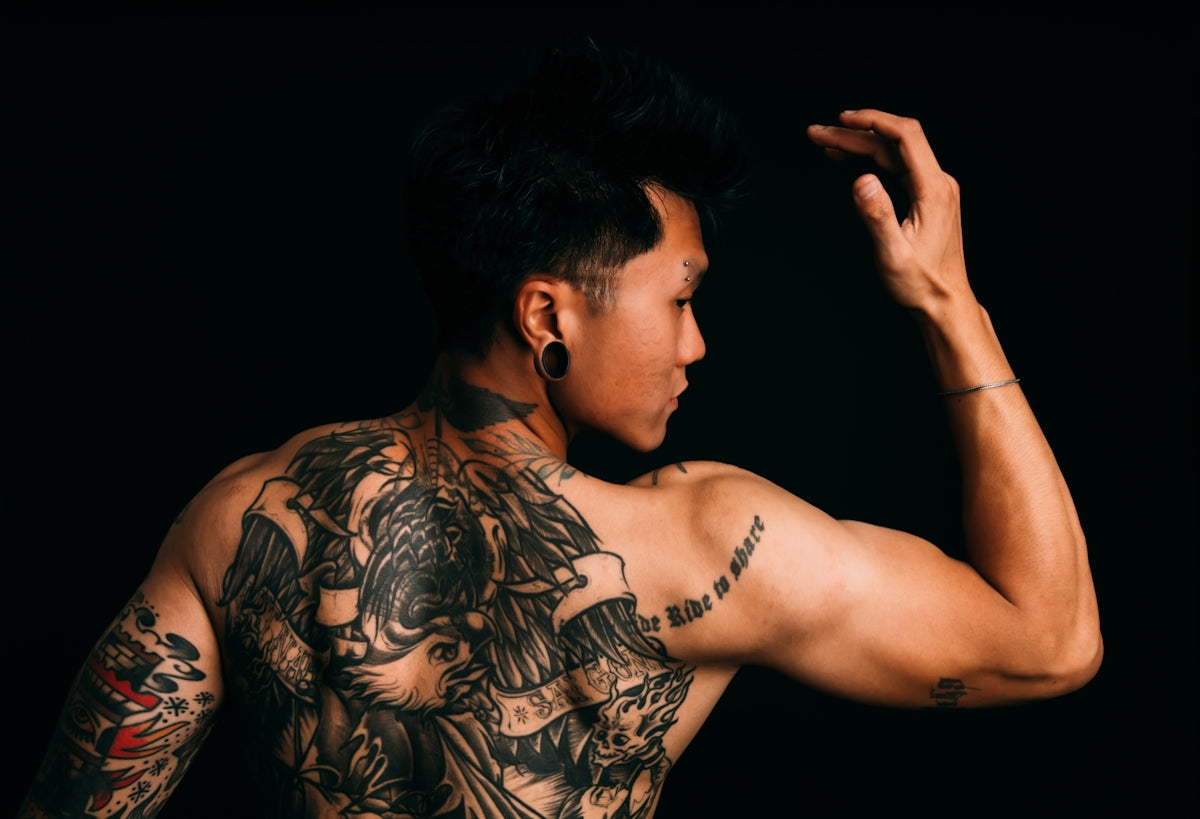 Man with extensive back tattoos flexing arm